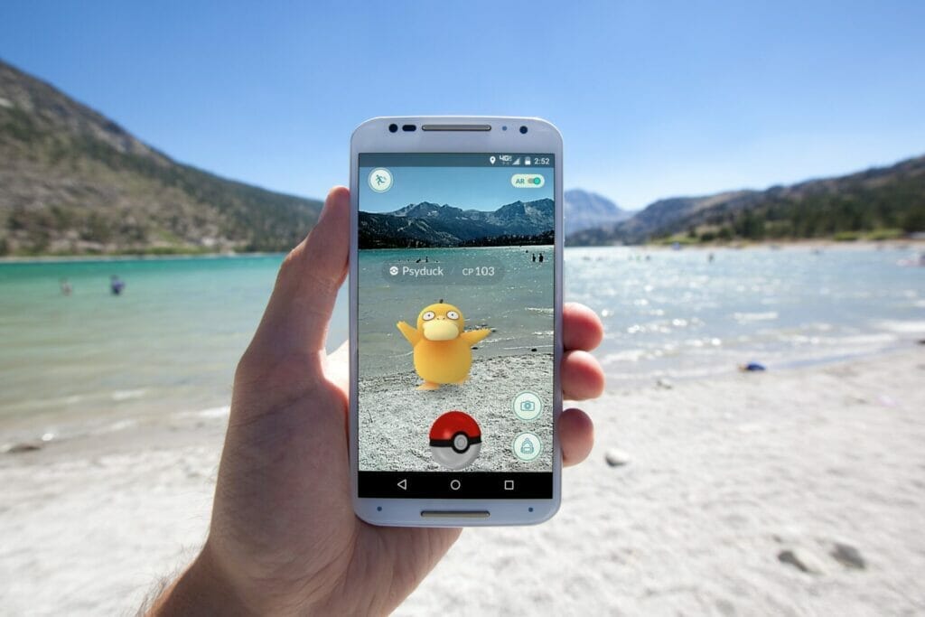 Eine Hand, die am Strand ein Smartphone zeigt, auf welchem Pokémon Go läuft.
