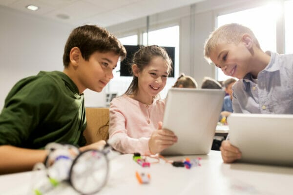 Drei Kinder nahmen an einer gemeinsamen Lernaktivität mit Tablets teil, um in einem hell erleuchteten Klassenzimmer Programmieren und Lernspielzeug zu erlernen.
