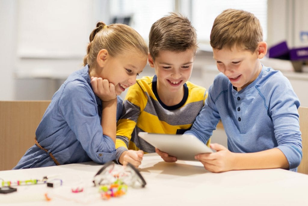 Ein Mädchen und zwei Jungen schauen sich Programmiercode auf einem iPad an.