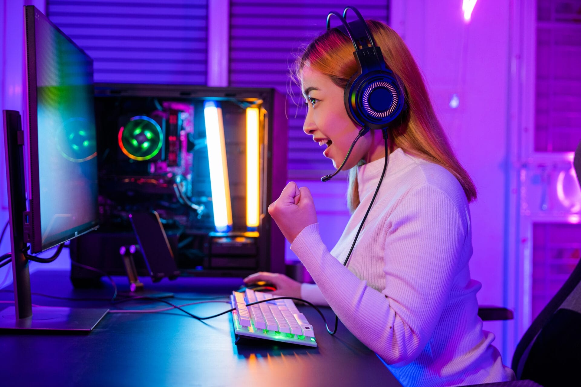 Gewonnener Sieg. Gamer Mädchen spielt Online-Videospiel aufgeregt auf Desktop-Computer PC bunte Neon-LED-Lichter, Frau in Gaming-Kopfhörer verwenden Computer sie glücklich erfolgreich, E-Sport-Konzept, Seitenansicht