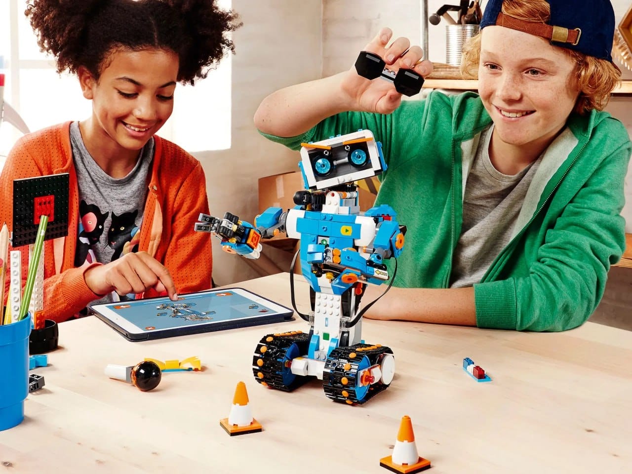 Zwei Kinder bauen und programmieren einen Lego Boost Roboter, den sie aus Bauklötzen gebaut haben. Auf dem Tisch liegen ein Tablet und verschiedene Kleinteile.